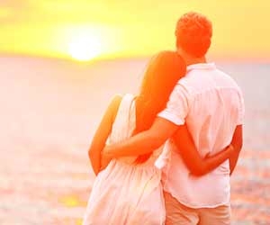A romantic couple holds each other while watching sunset on beach