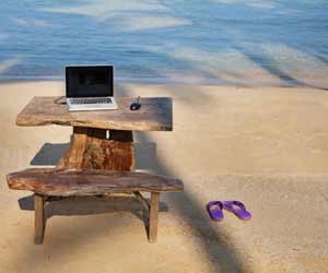 Flexible work station with laptop on wooden desk at beach.