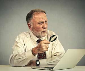 Older job seeker using a magnifying glass to look at laptop