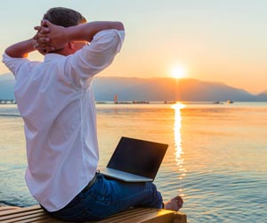 Remote worker with laptop sitting on dock watching sunset