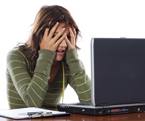 A frustrated job seeker with hands on head in front of laptop