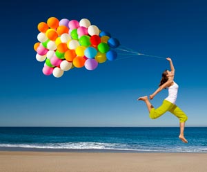 Happy woman jumping on beach with string of helium balloons