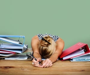 Bored woman lying with head on desk surrounded by work