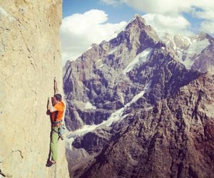 An adrenaline junkie climbing a sheer rock face with a mountain in the background