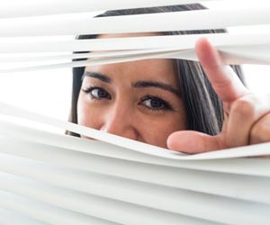 Woman peeking through blinds and looking out of a window