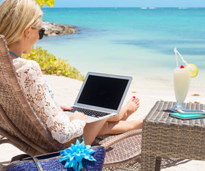 Woman on tropical beach working from her laptop sipping a fancy drink.