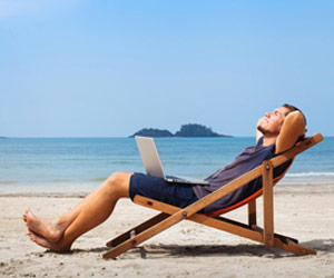 Man relaxing in a lounge chair on a beach with a laptop on his lap